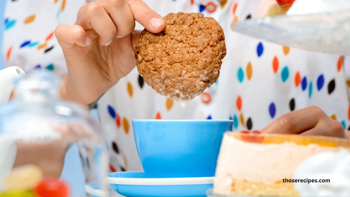 Freshly baked madeline cookies with a golden brown shell-like shape, dusted with powdered sugar, arranged on a wooden table alongside a whisk and bowl of cream.