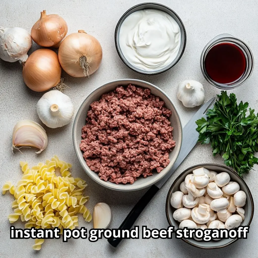 Fresh ingredients for ground beef stroganoff including ground beef, sliced mushrooms, onions, garlic, sour cream, Worcestershire sauce, egg noodles, and beef broth on a kitchen counter.